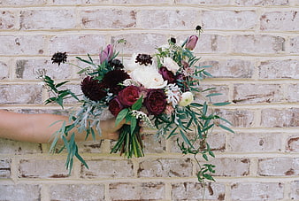 Hand Holding Dark Moody Wedding Bouquet Against Brick Wall