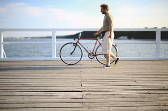 Man walking with red bicycle on wooden pier by water