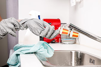 Hands in gray gloves cleaning kitchen sink with cloth