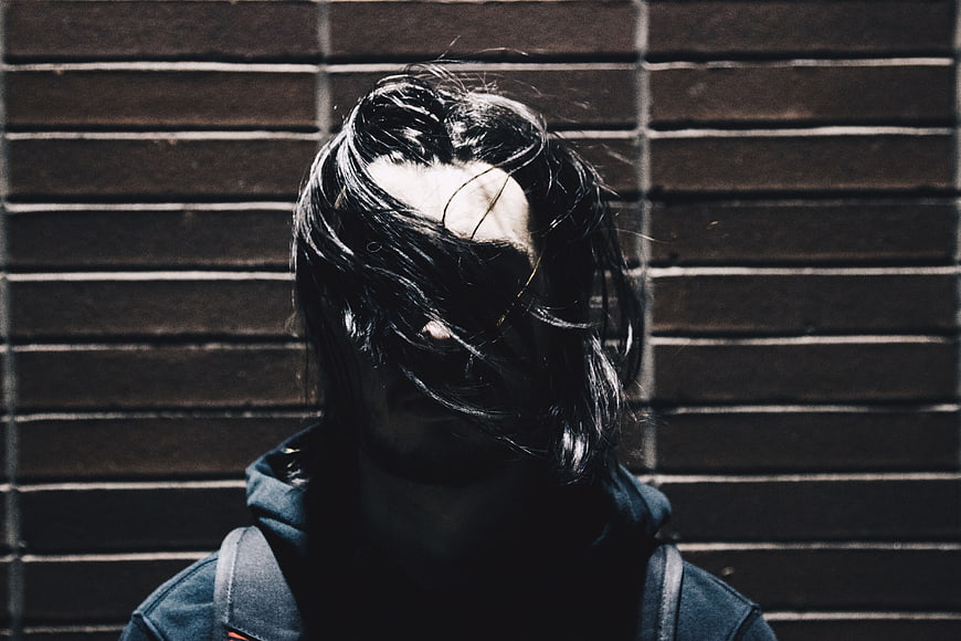Moody Portrait of Person with Hair Covering Face Against Brick Wall