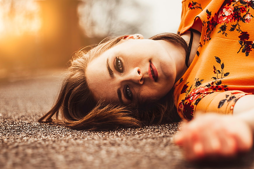 Sad woman lying on asphalt road looking at camera