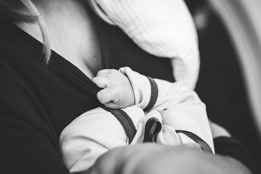Close-up of baby hand holding mother's shirt while breastfeeding