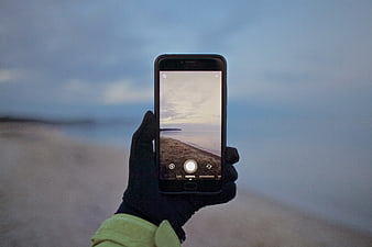 Hand holding smartphone taking photo of beach at dusk