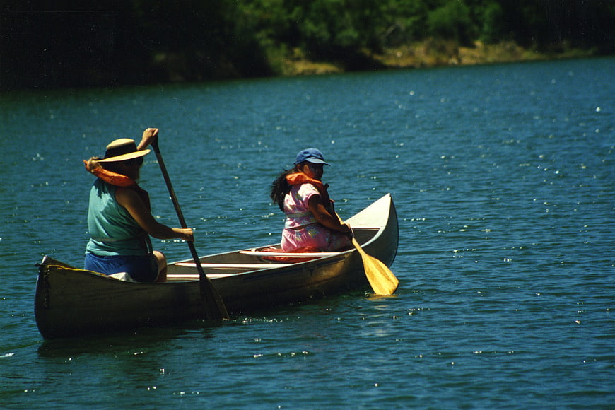 Two women paddling a canoe on a sunny lake