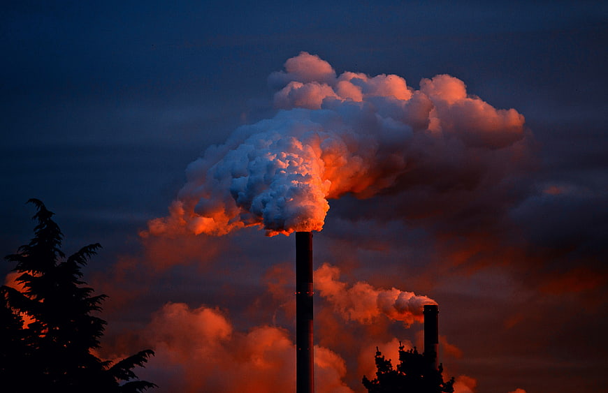 Industrial smokestacks emitting plumes against a dramatic sunset sky