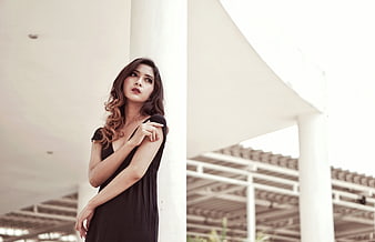 Woman in Black Dress Leaning Against White Pillar