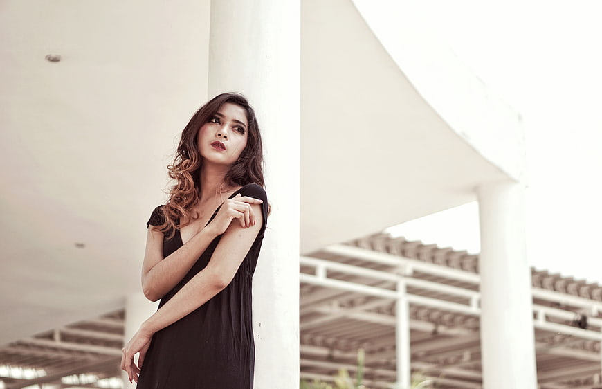 Woman in Black Dress Leaning Against White Pillar