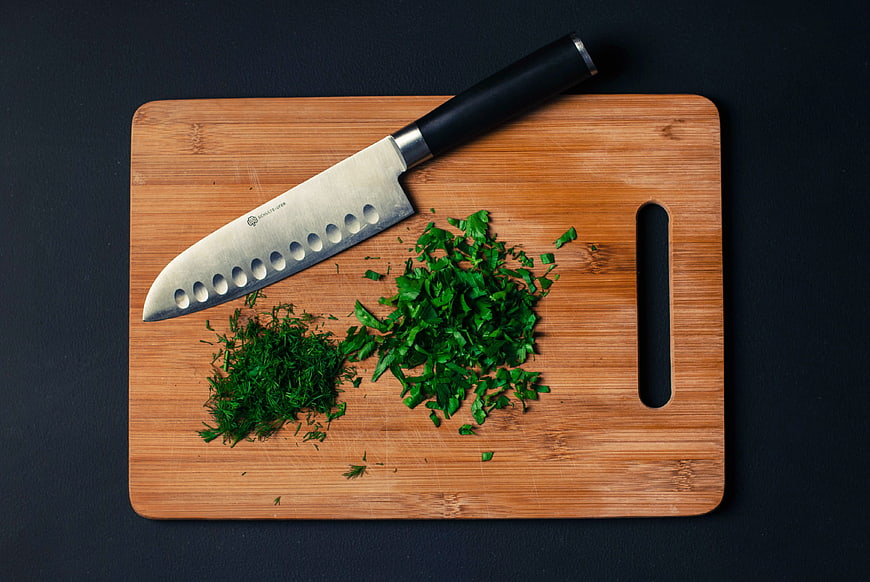 Chopped parsley and dill on wooden cutting board with knife