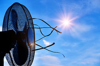 Electric fan silhouette with ribbons against bright summer sun and blue sky