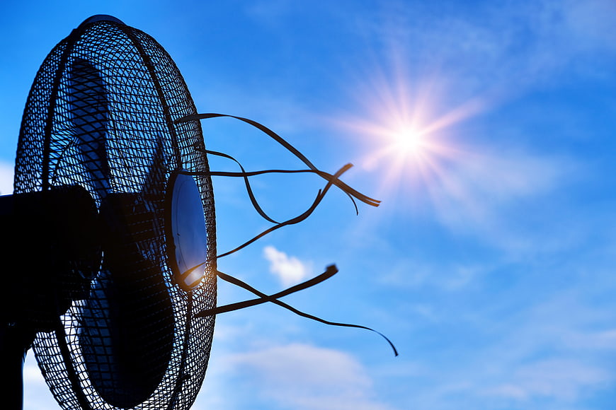 Electric fan silhouette with ribbons against bright summer sun and blue sky