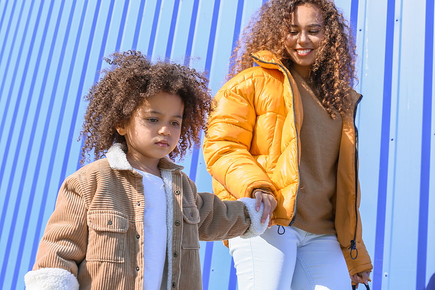 Mother and daughter holding hands against blue striped wall