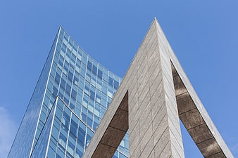 Modern Glass Skyscraper and Concrete Arch Against Blue Sky