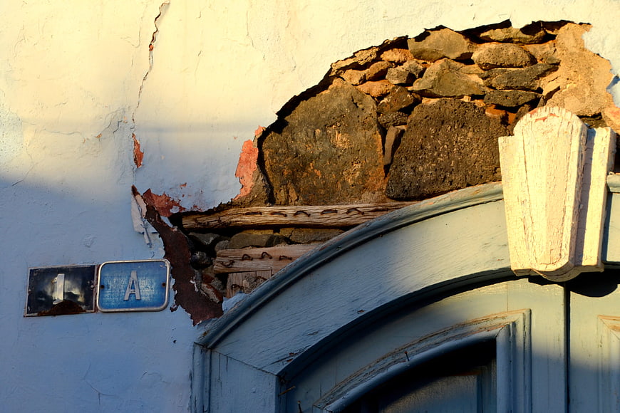 Dilapidated wall with exposed stone and blue door frame