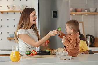 Happy mother feeding toddler cucumber in modern kitchen