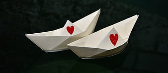 Two white paper boats with red hearts on dark water