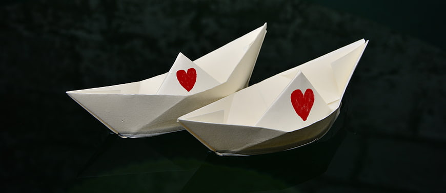 Two white paper boats with red hearts on dark water
