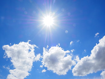 Bright Sun With Starburst Rays And Fluffy White Clouds In Blue Sky