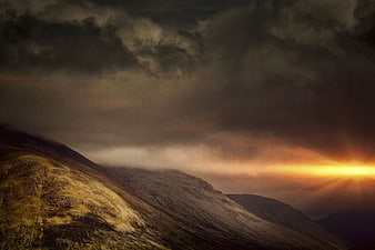 Dramatic sunset over rugged mountain highlands with storm clouds