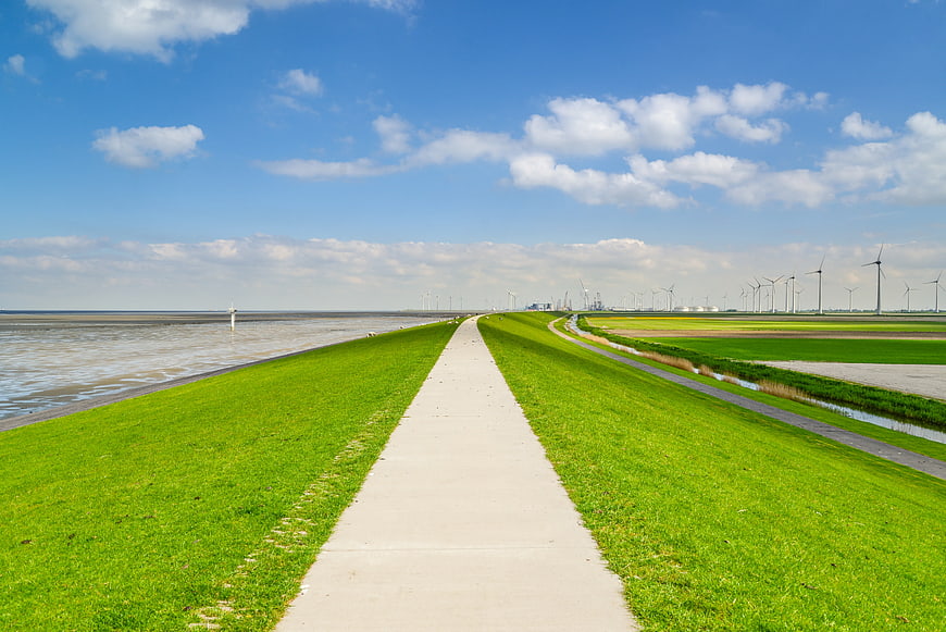 Concrete Path Along Green Dike with Wind Turbines