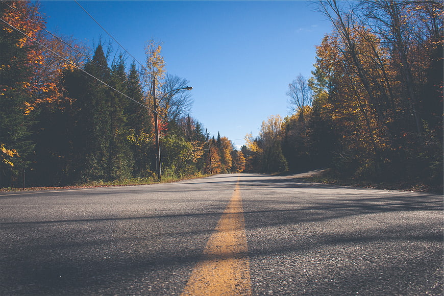 Empty asphalt road with yellow line through autumn forest