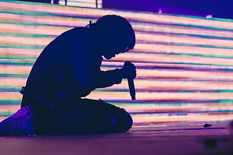 Silhouette of singer kneeling on stage with microphone
