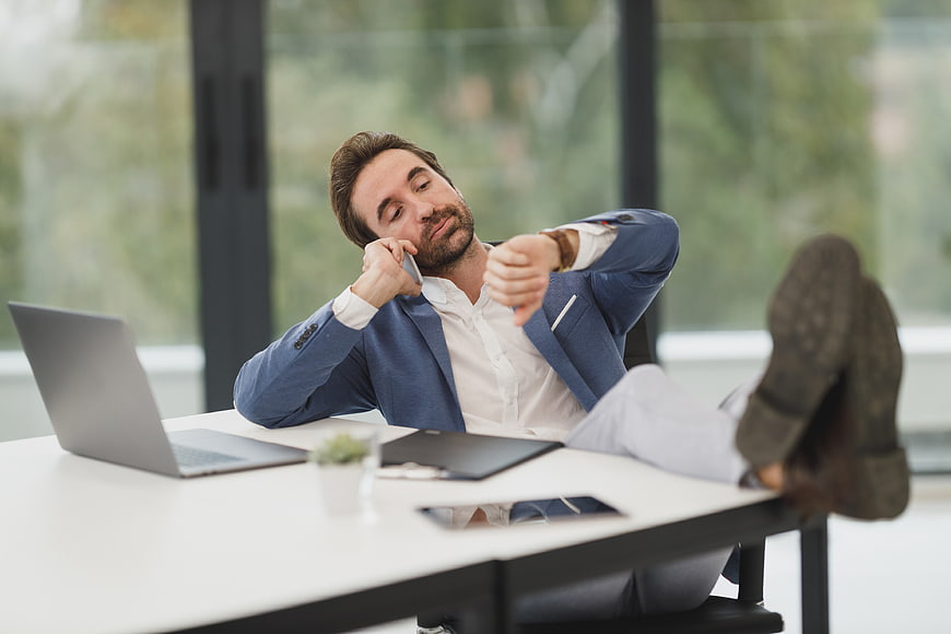 Bored businessman checking watch with feet on desk