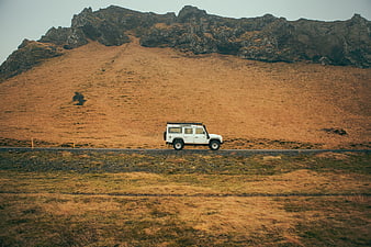 White SUV driving on rural road with mountain backdrop