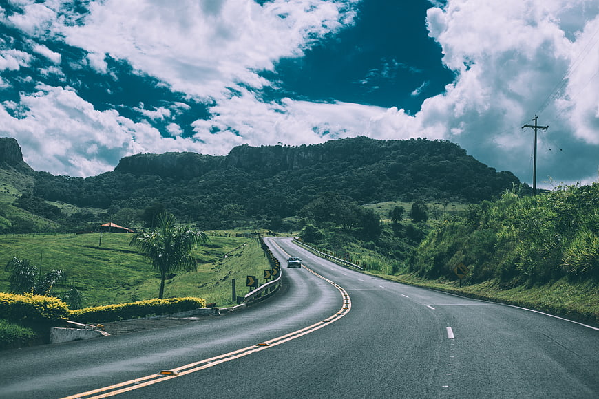 Winding Highway Through Green Hills Under Dramatic Cloudy Sky
