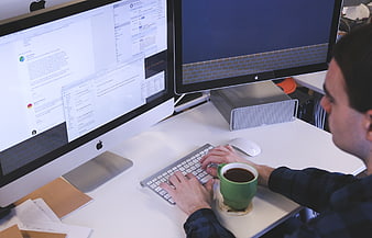 Man Typing at Dual Monitor Workspace with Coffee