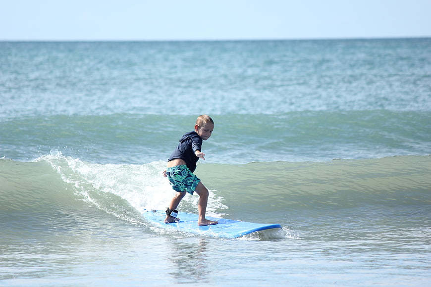 Young boy surfing on a blue board in the ocean