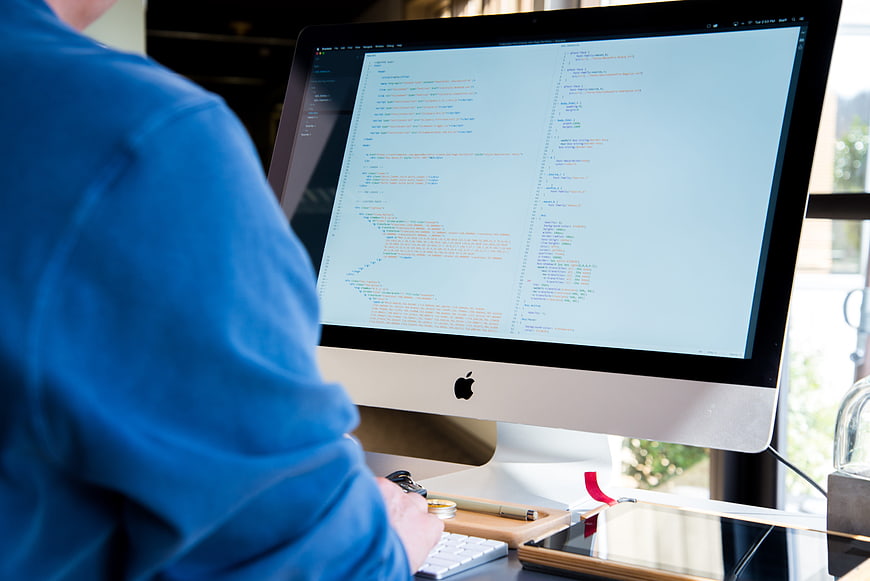 Programmer coding on iMac in modern office workspace