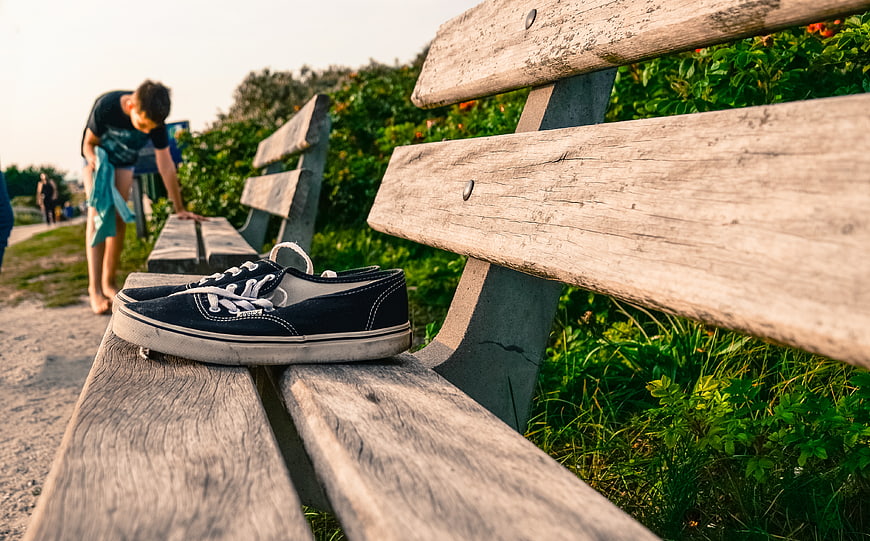 Black canvas sneakers on a wooden park bench with blurred background
