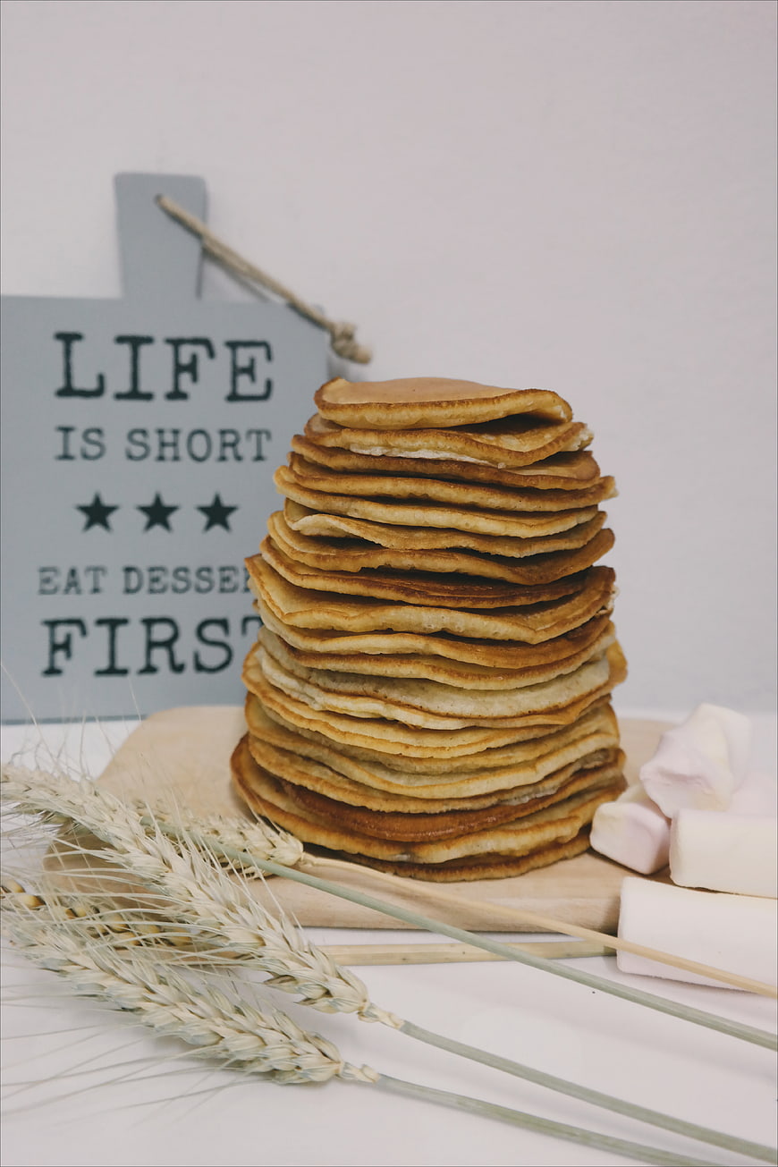 Stack of pancakes with marshmallows and wheat on wooden board