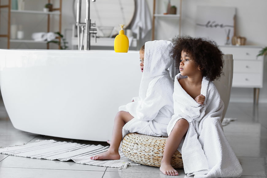 Two children in white towels sitting in modern bathroom