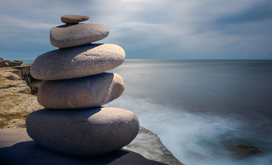 Stacked Zen Stones on Rocky Coastline with Ocean Background