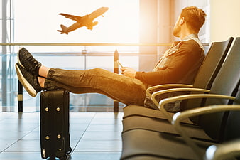 Relaxed male traveler resting in airport lounge with rolling suitcase
