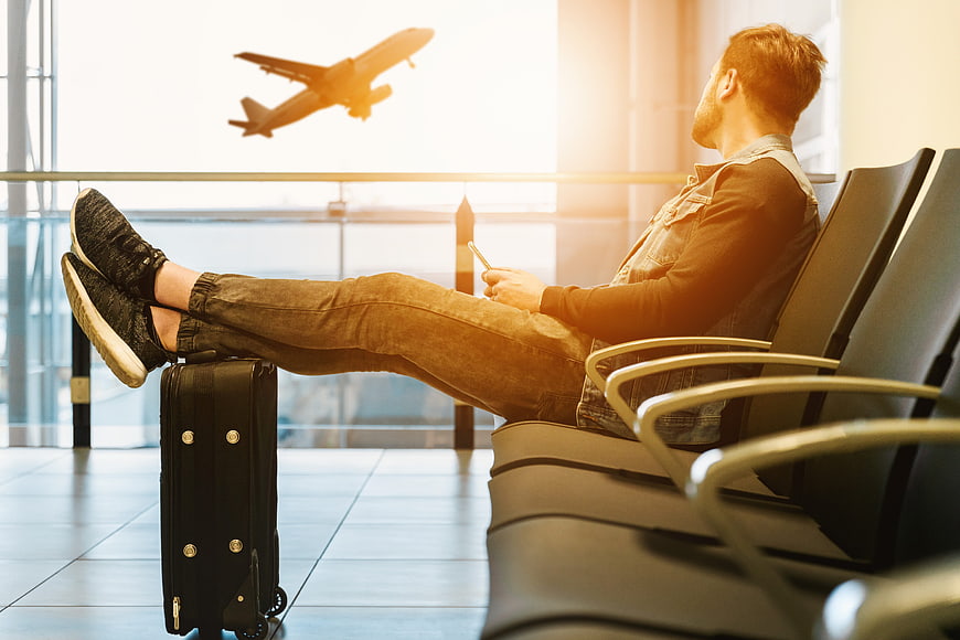 Relaxed male traveler resting in airport lounge with rolling suitcase