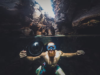 Underwater split-level shot of bearded man swimming in rocky cave
