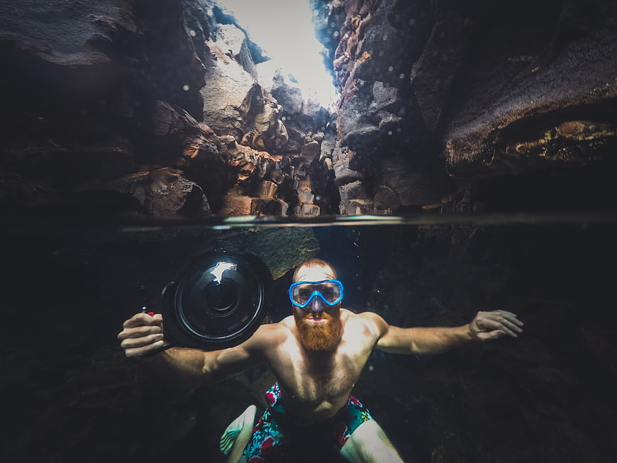 Underwater split-level shot of bearded man swimming in rocky cave