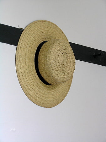 Woven straw hat hanging on black wooden rack against white wall
