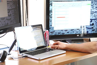 Office workspace with laptop, monitors, and energy drink