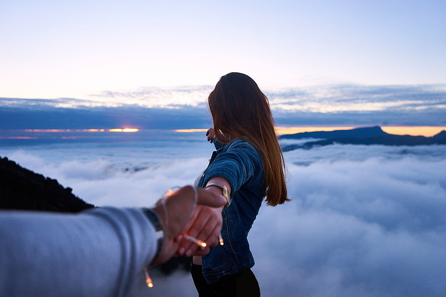 Couple holding hands above clouds at sunset mountain view