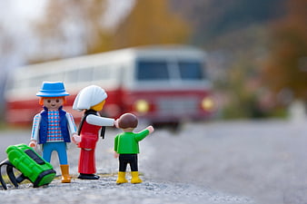 Toy family figures waiting for a red bus on a road