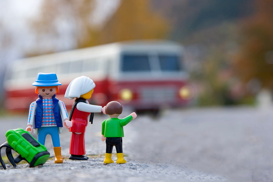 Toy family figures waiting for a red bus on a road
