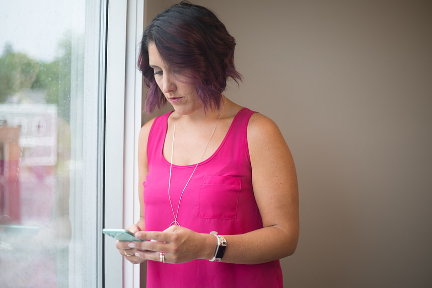 Woman with purple hair texting on smartphone by window