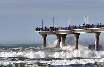 Ocean pier with crashing waves and tourists