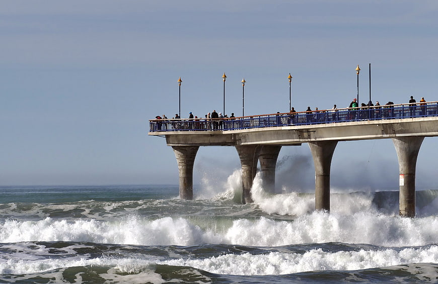Ocean pier with crashing waves and tourists