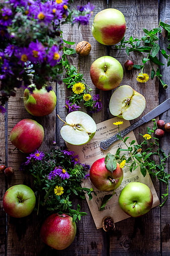 Rustic still life with apples, flowers, and sheet music on wood