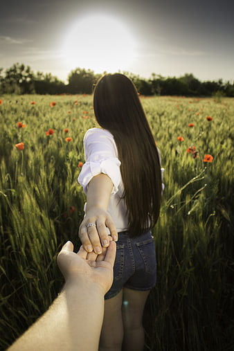 Couple holding hands in a wheat field with red poppies at sunset