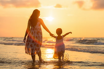 Mother and daughter walking on beach at sunset